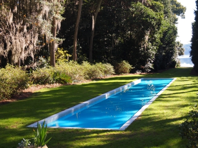 [Long, narrow, shallow, cement pool with very blue water built in a clearing leading to a view of Lake Hall.]